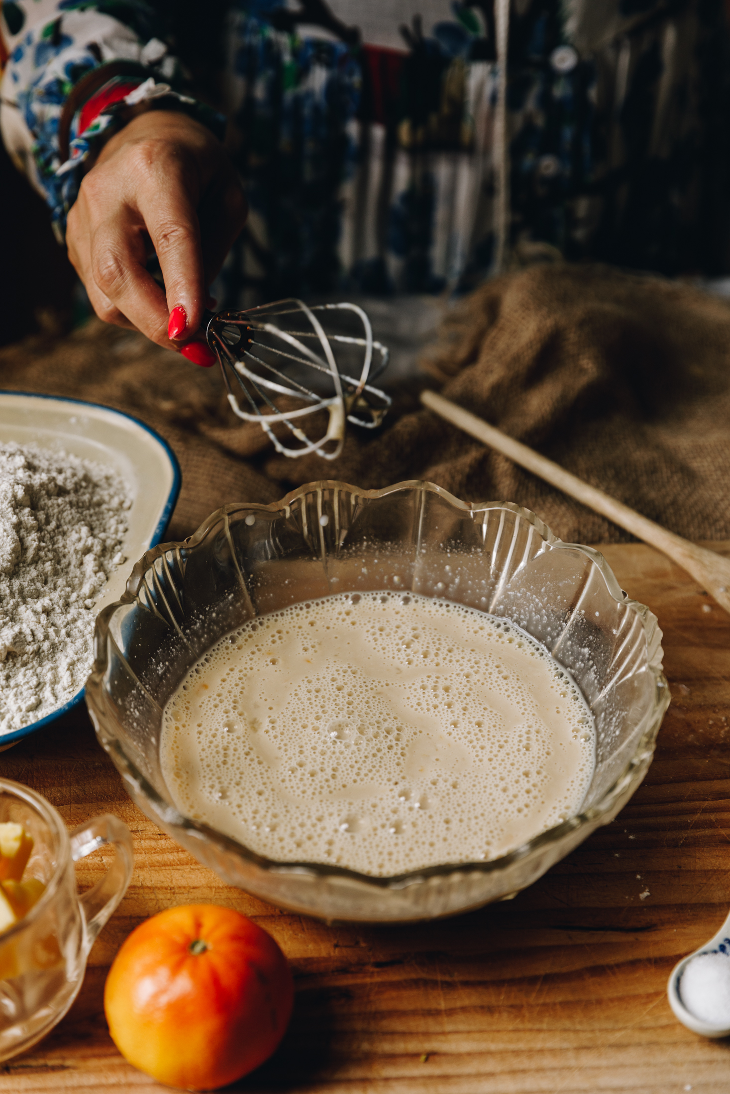 A bowl of activated yeast sits on a wooden table. The yeast is lightly foamy and rising to the top of the water.
