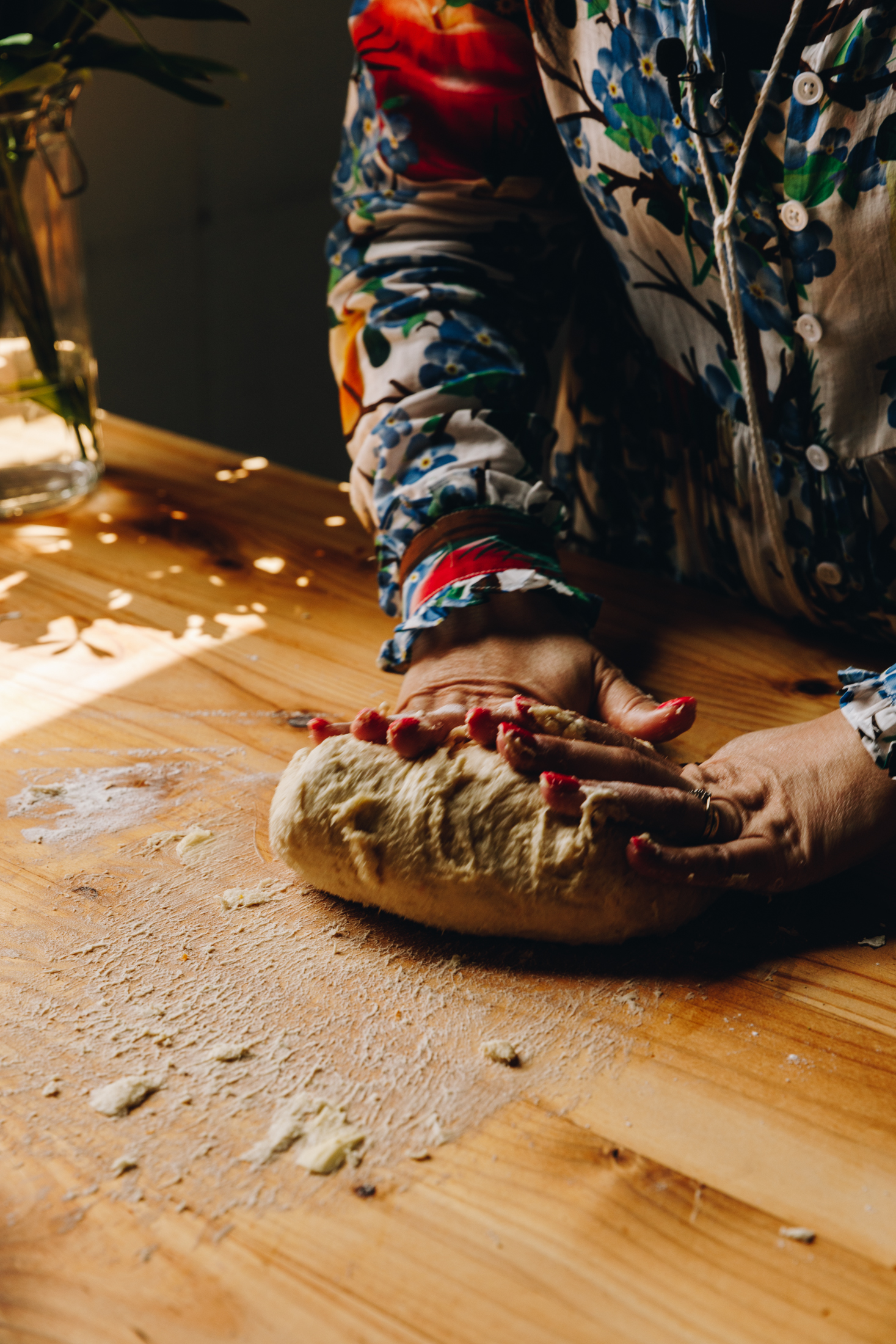 A sticky dough is being kneaded on a wooden table. Hands are seen kneading the dough.