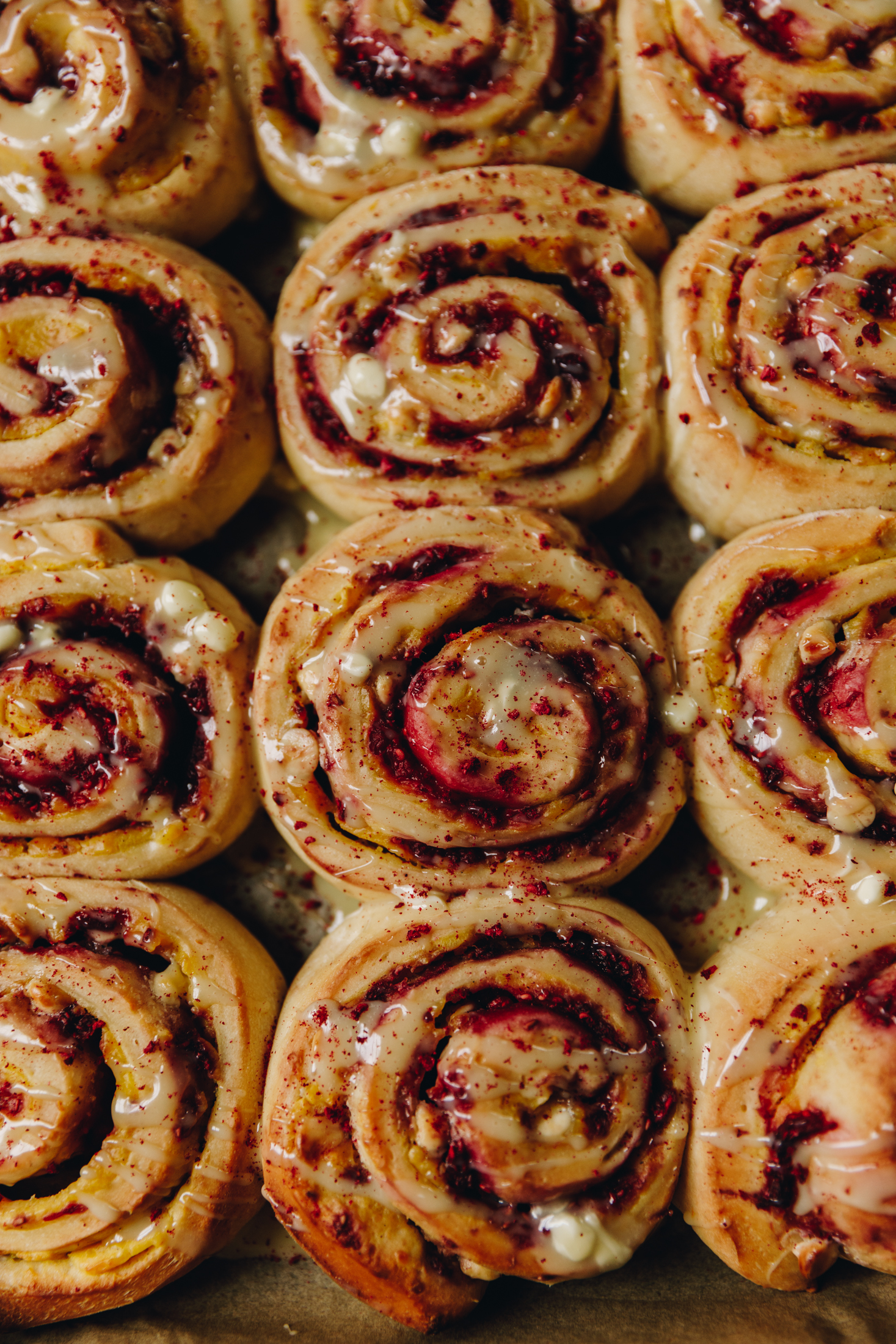 a tray of baked custard and raspberry scrolls show the texture of each one and the raspberry and white chocolate is seen. 