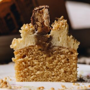 A Brown Butter Vanilla Cupcake has been sliced open to reveal the cake, gooey caramel centre, cream cheese frosting and snickers top.