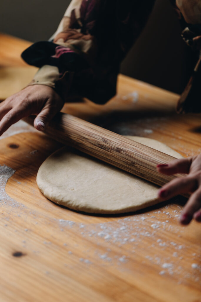 The Sweet Lemon Pastry is being rolled out on to a wooden table with a wooden rolling pin being used with two hands in shot. 