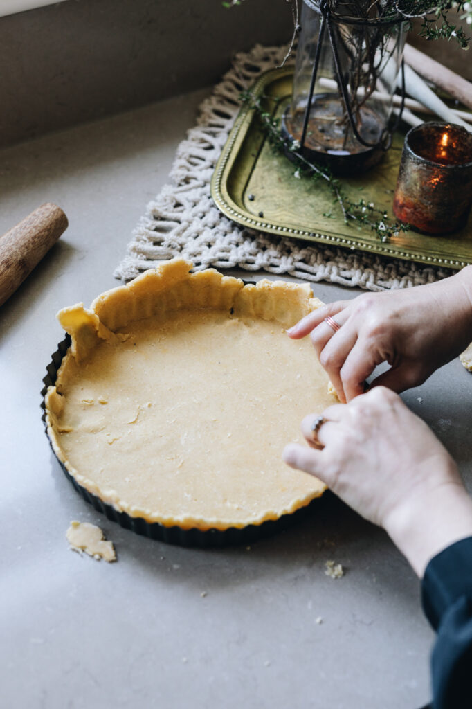 The sweet Lemon Pastry is being pressed in to a quick tin. Hands are pressing the dough in to the curves of the tin.