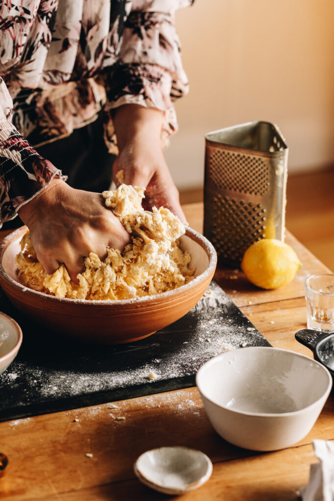 The Sweet Lemon Pastry is being kneading in the bowl with a hand kneading it. The hand is full of dough and flour is scattered around the edge. 