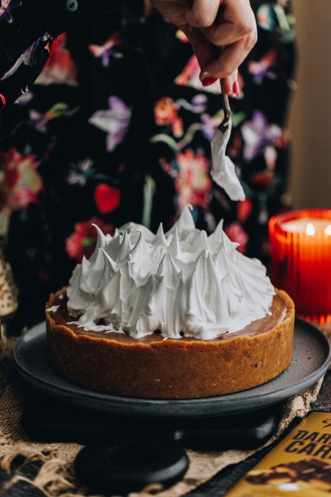 The How to Make Italian Meringue is being swept upwards on top of a S'mores Cheesecake. It looks like meringue flames as they move in different directions.