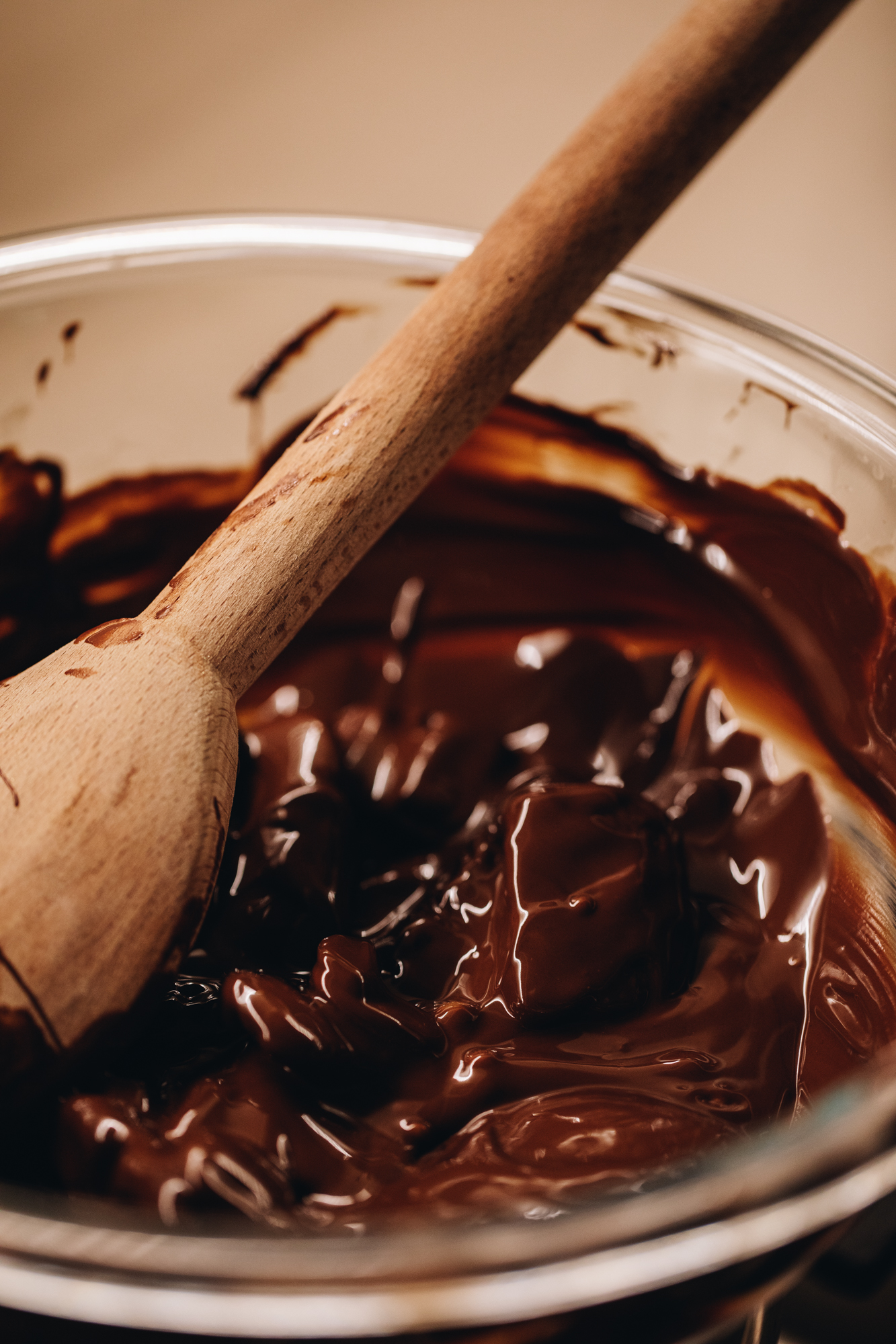 Melted chocolate is in a glass bowl with a wooden spoon in it.