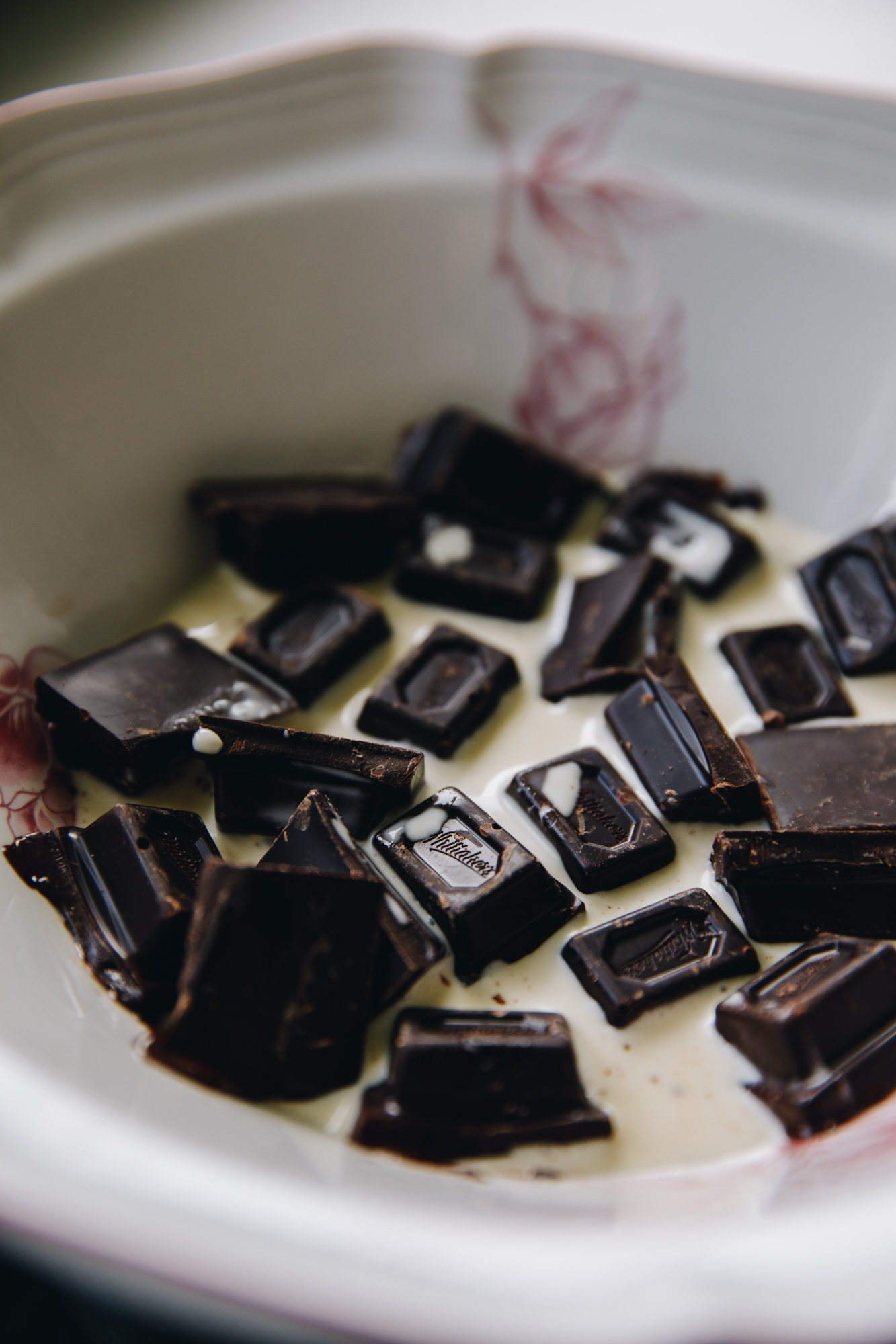 In a white bowl with pink flowers is pieces of dark chocolate in cream.