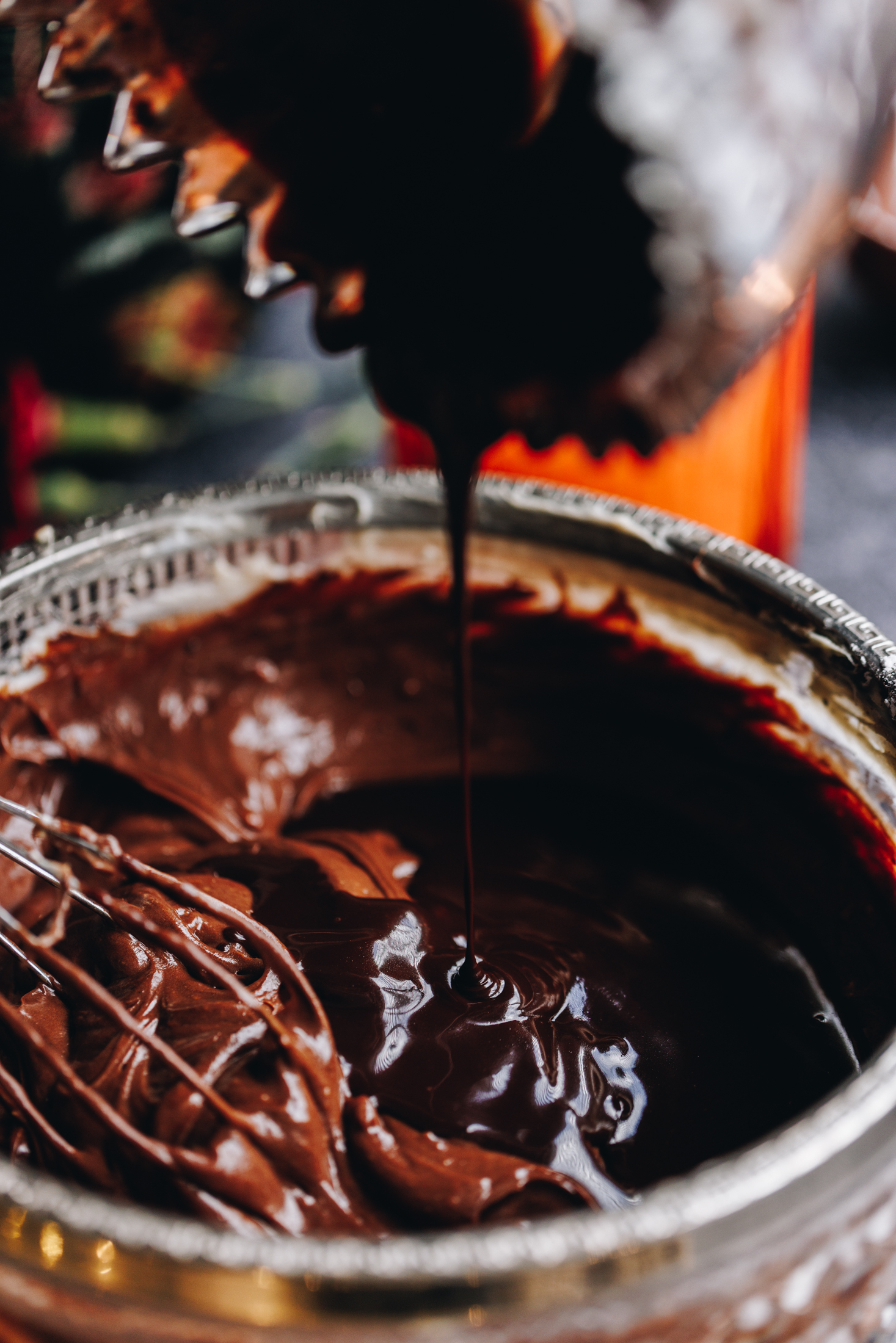 A glass bowl has a chocolate mixture in it, pour in to the bowl is melted chocolate.