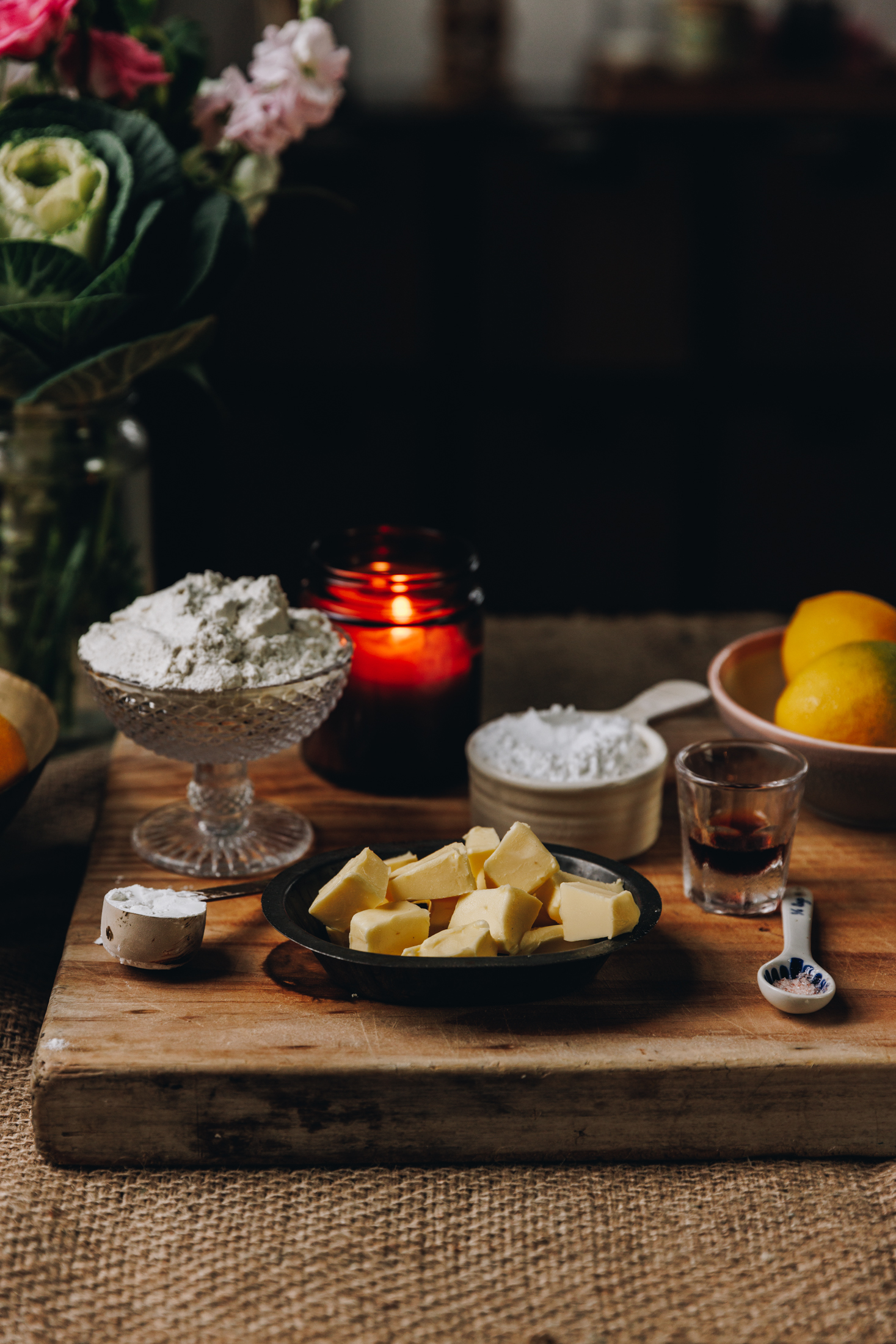 Placed on a wooden shopping is a dark amber candle and vintage dishes and cutlery that are holding the ingredients for the Homemade Lemon Meringue Pie.