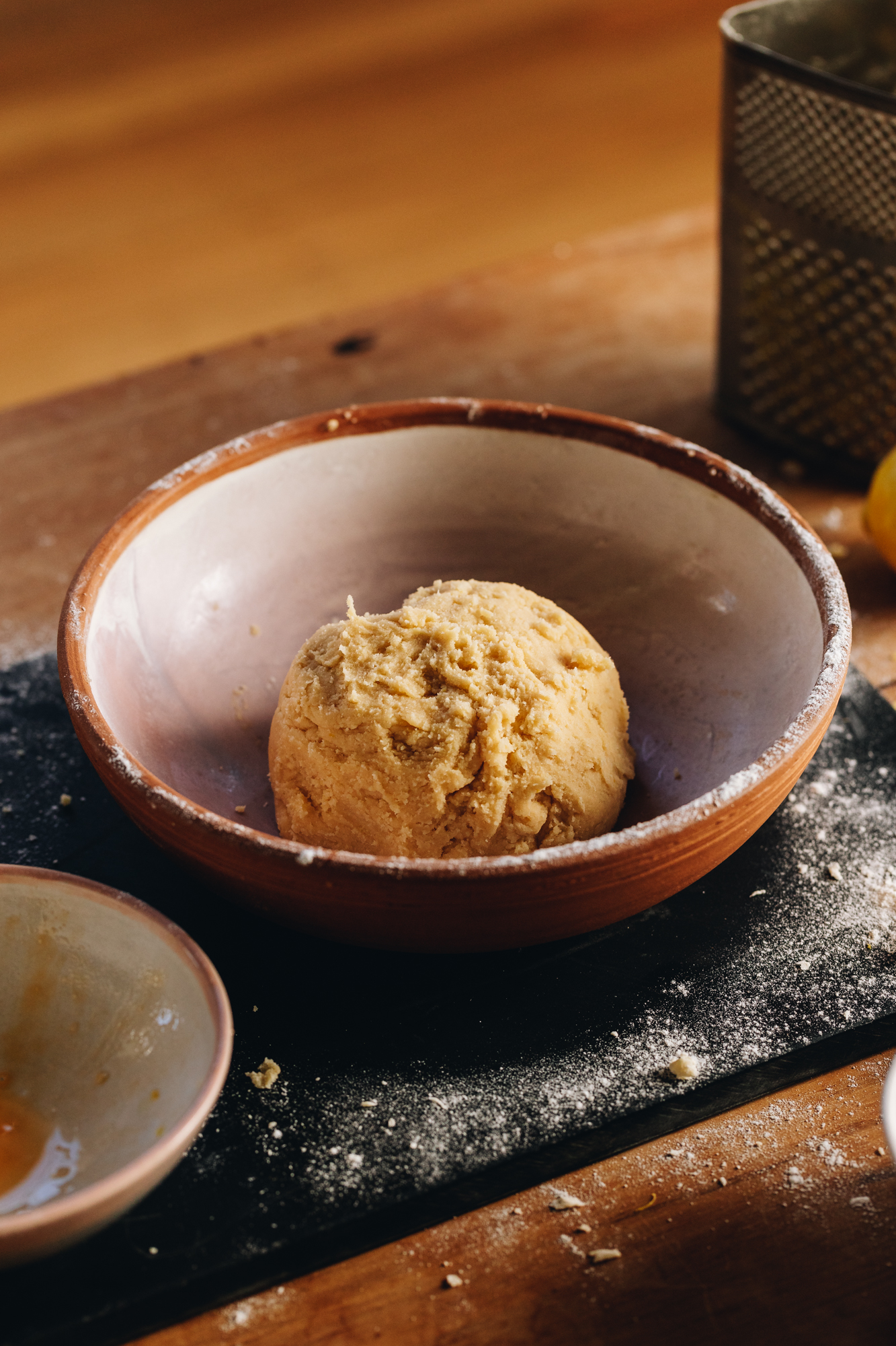 The Sweet Lemon Pastry has been been worked in to a ball and is sitting in the centre of a clay bowl. The bowl is sitting on a flour dusted black board. 
