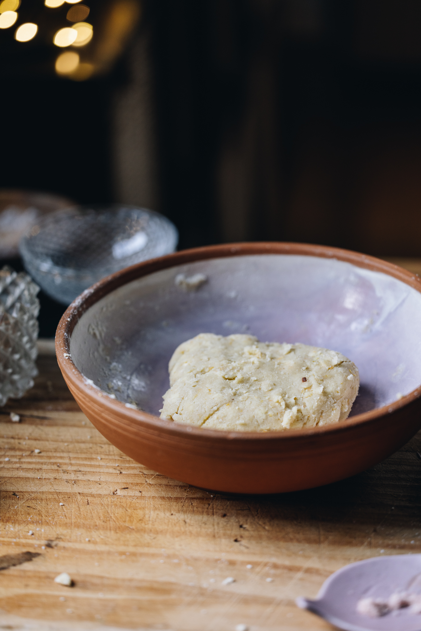 A ceramic bowl sits on a wooden bench. It has a fresh pastry sitting inside it. Empty glasses are behind the bowl.