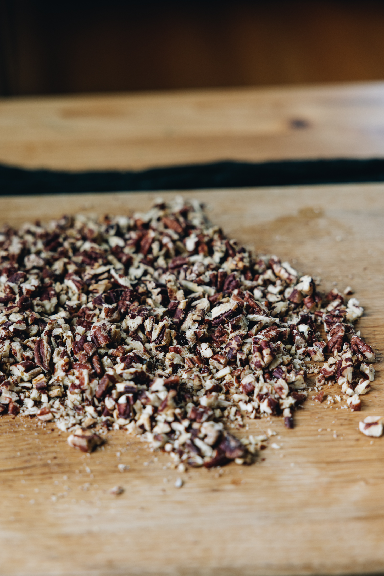 On a wooden board sits a large pile of chopped pecan nuts.