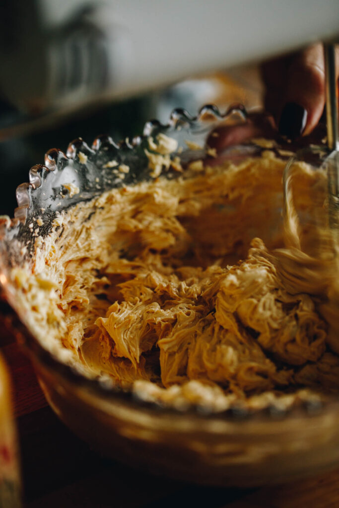 Close up of The Peanut Butter Weetbix Slice peanut butter buttercream being whipped with a white hand mixer. It is an action shot of the butter being whipped. 