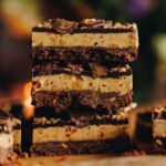 Close up of three pieces of peanut butter weetbix slice in a pile on top of each other. The slice is on brown paper.
