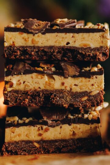 Close up of three pieces of peanut butter weetbix slice in a pile on top of each other. The slice is on brown paper.