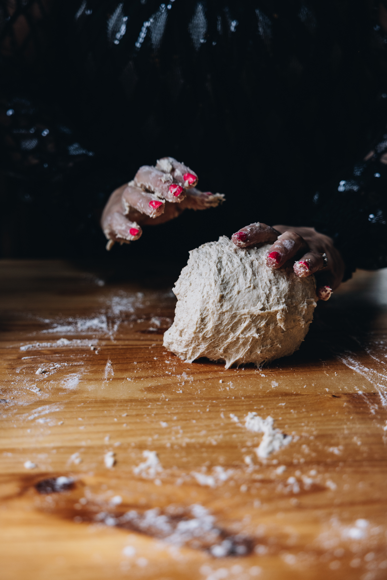A sticky dough is being kneaded on a wooden table. Hands are seen kneading the dough. 