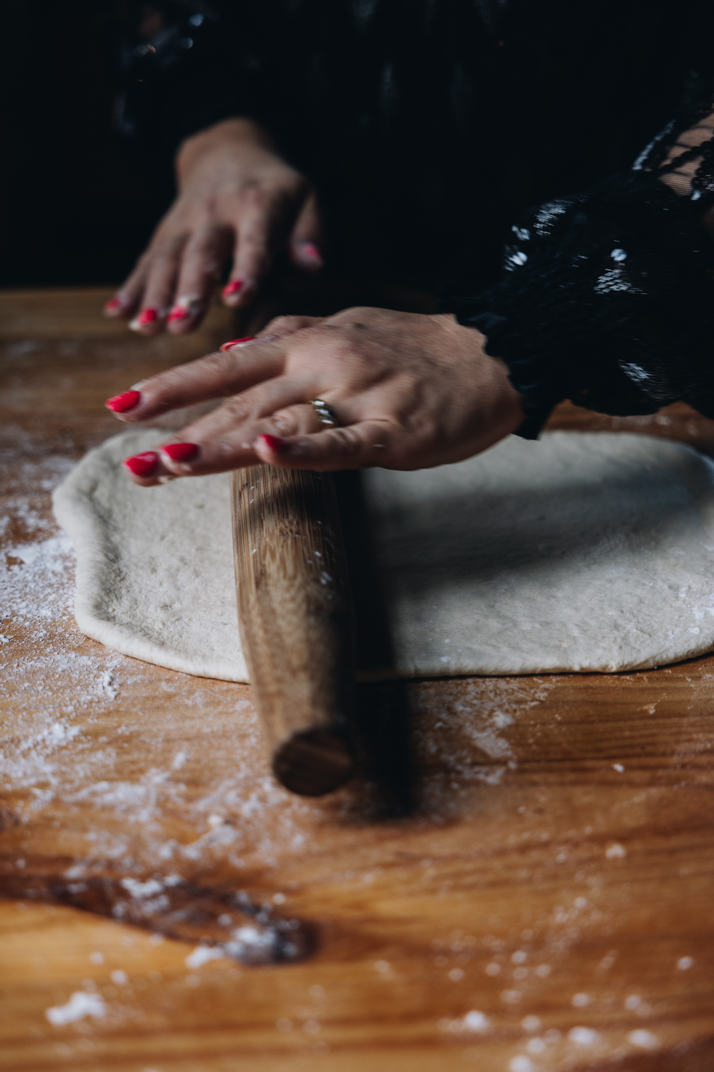 The Cheese and Pesto Dough is being rolled out on the table with a wooden rolling pin. Flour is visible all over the table. 