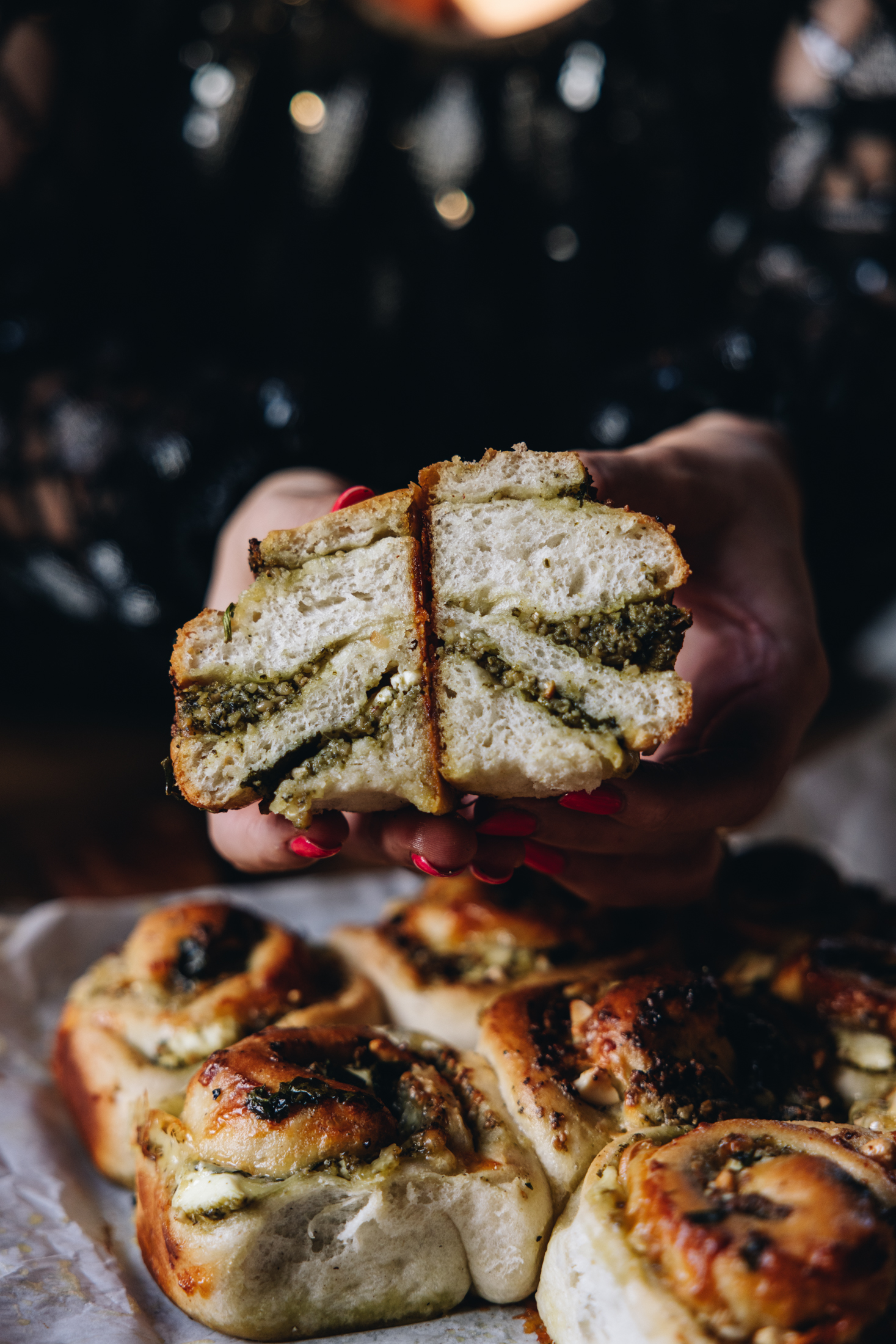 A freshly baked cheese and pesto scroll has been cut open to reveal the soft bread and pesto running through it. 