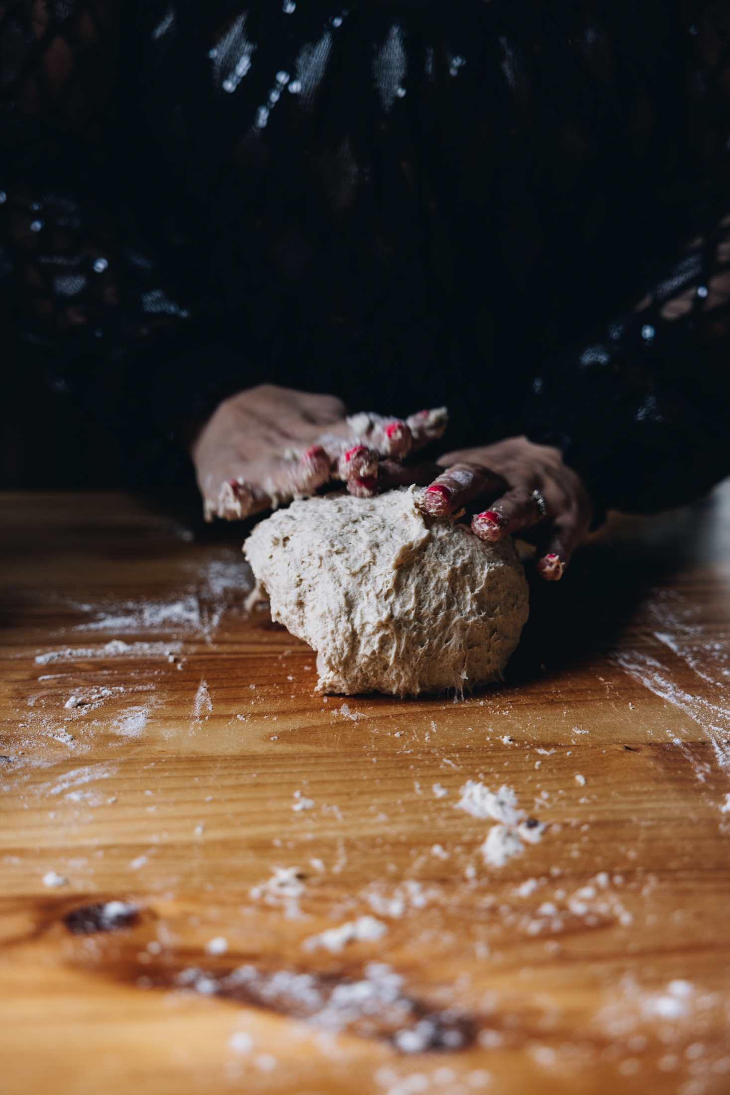 A sticky dough is being kneaded on a wooden table. Hands are seen kneading the dough.