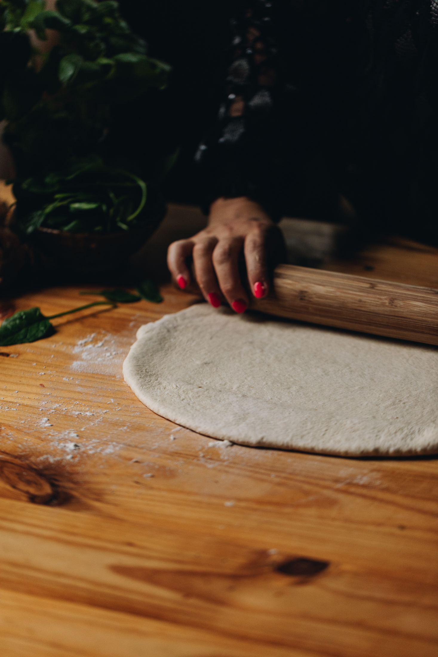 The Cheese and Tomato Dough is being rolled out on the table with a wooden rolling pin. Flour is visible all over the table.