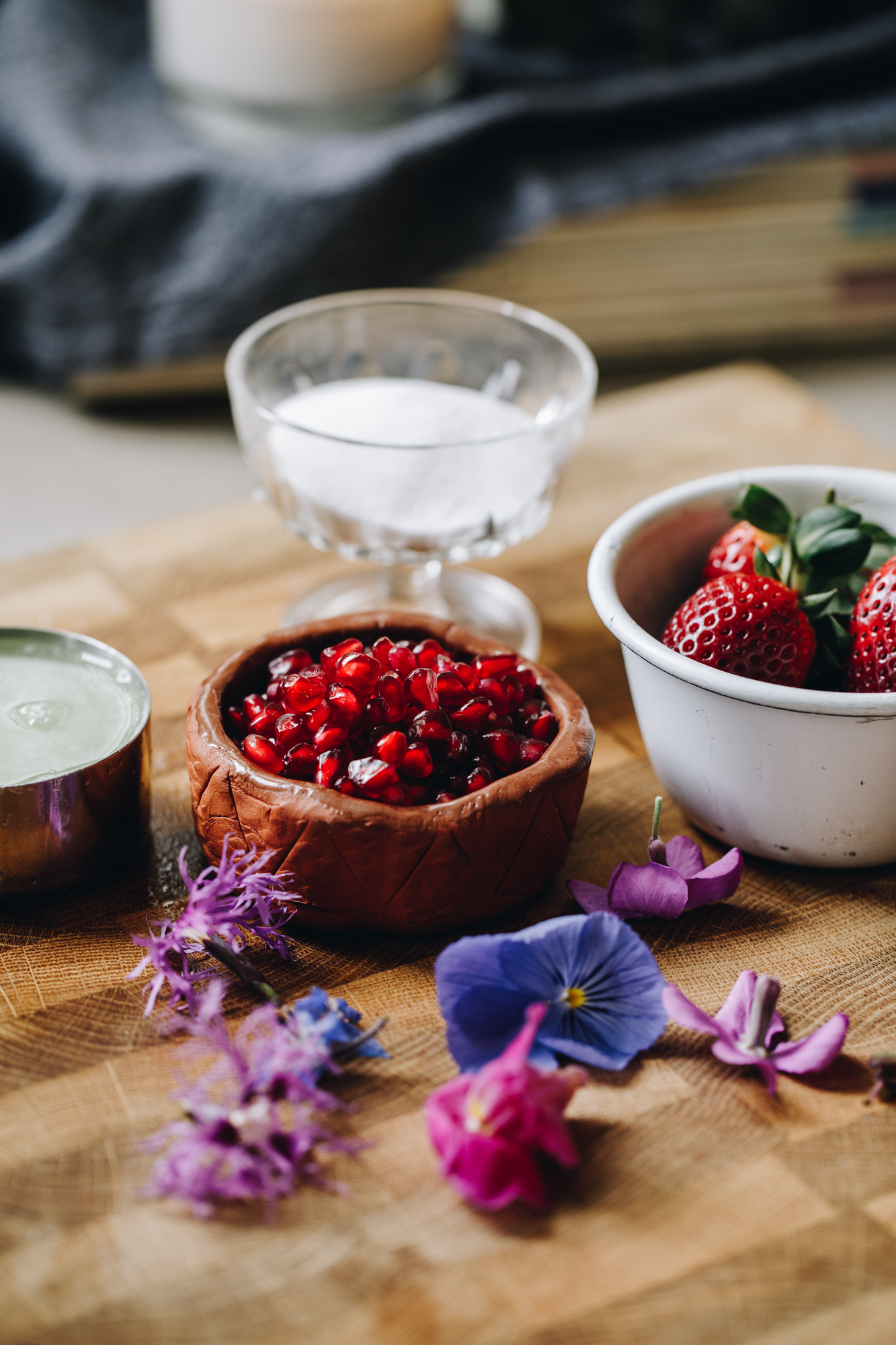 On a wooden board is vintage glasses showing pomegranate seeds, strawberries and edible flowers.