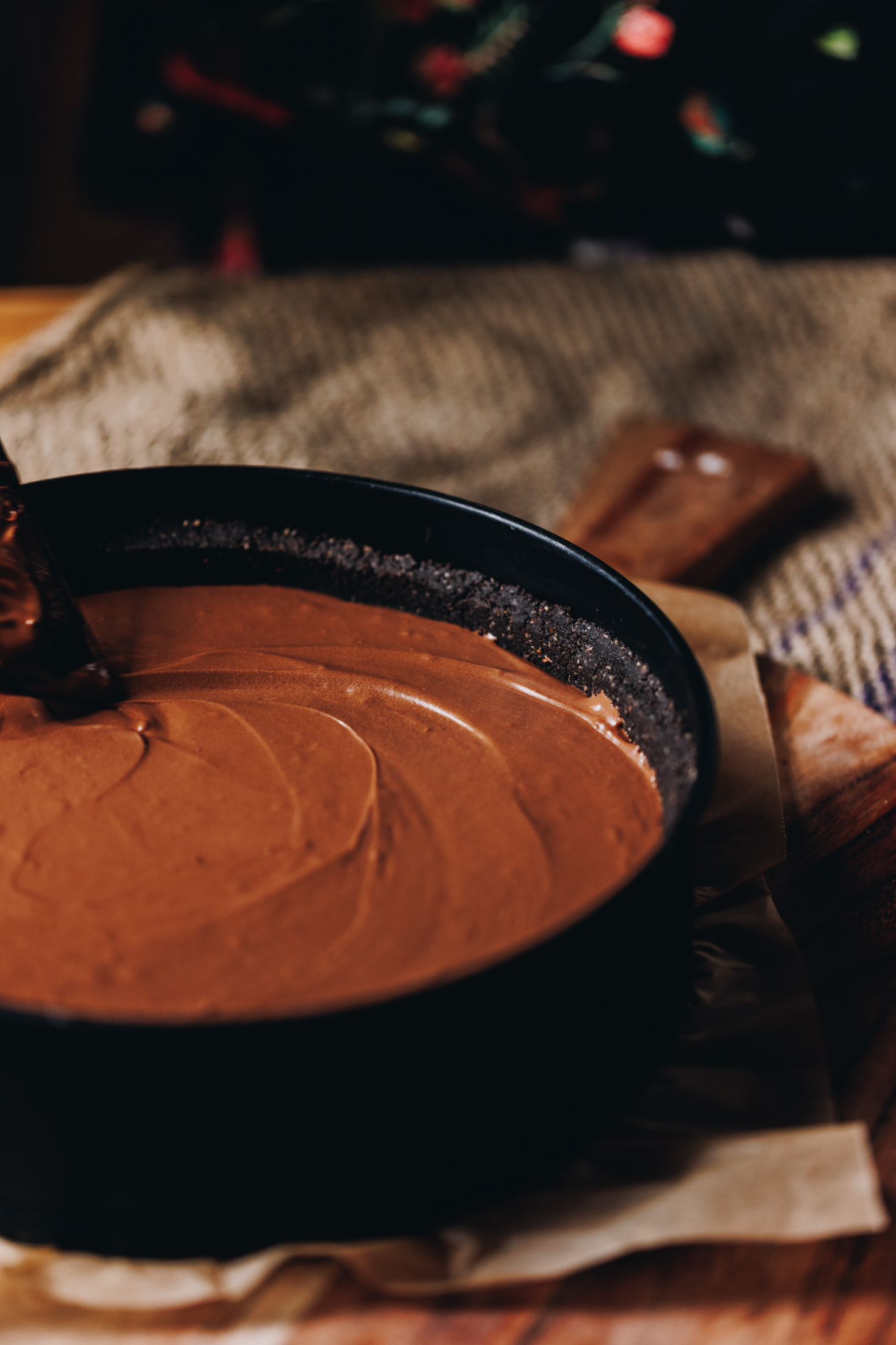 The chilled mocha cheese is being spread in to the black cake tin, it is sitting on a wooden board on a wooden table. 