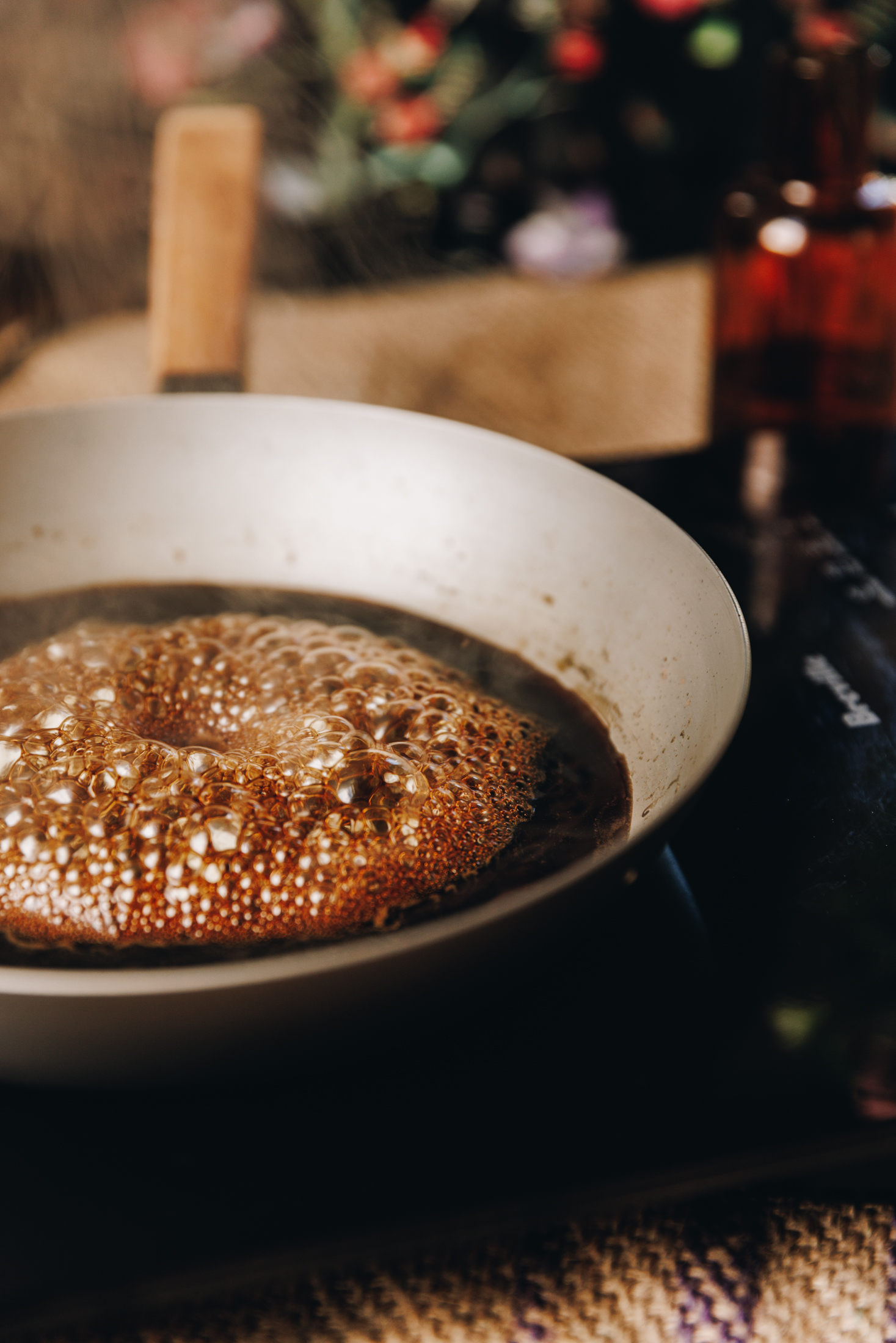 Coffe syrup is bubbling in a frying that is sitting on a black portable stove, on a wooden table. 