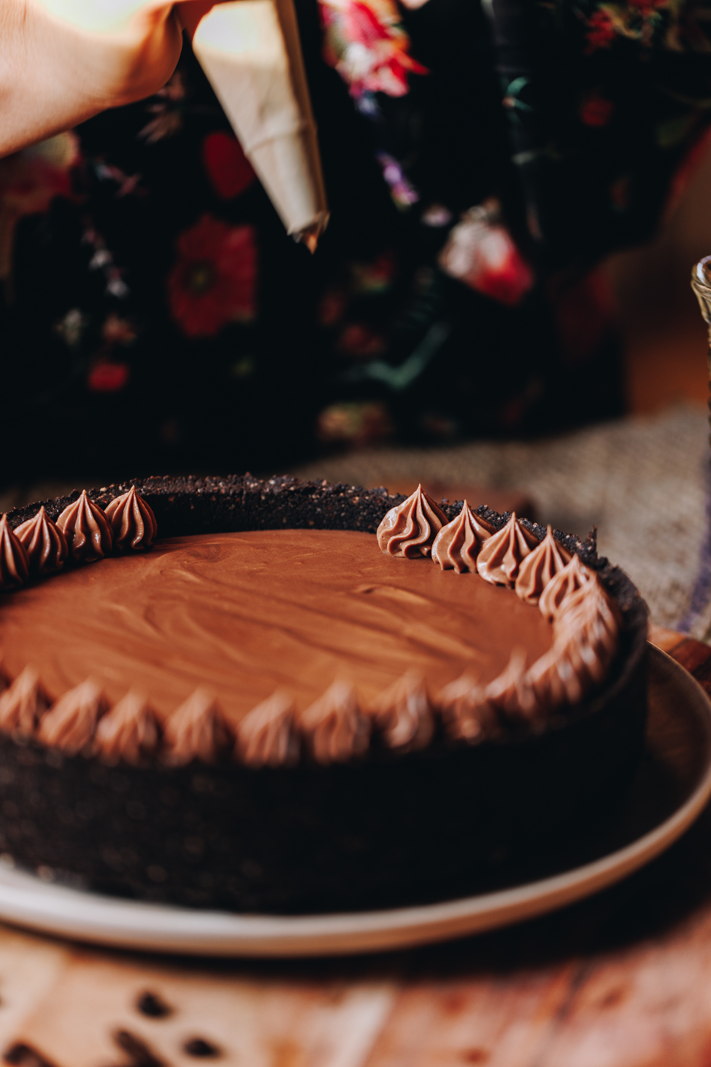 The chilled mocha cheese is being decorated with sour cream ganache in the black cake tin, it is sitting on a wooden board on a wooden table.