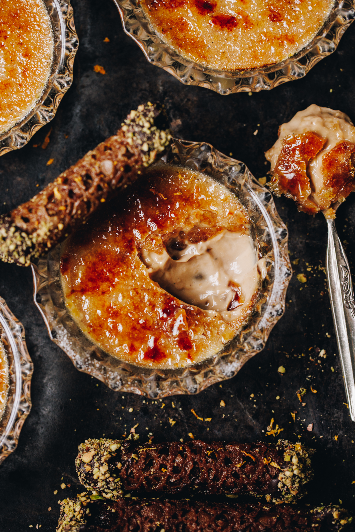 On a black tray is a flat lay of freshly baked chai creme brûlée - one of them has been cracked open, revealing the creamy custard underneath the hard sugar top. 