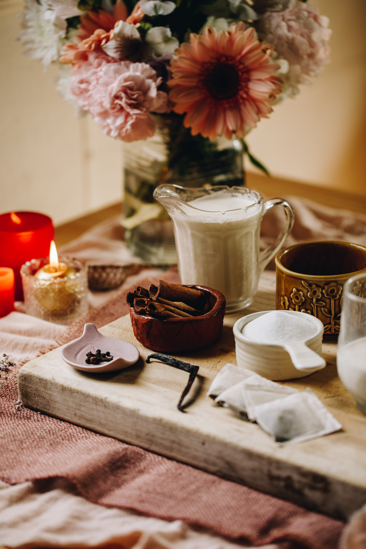 Chai Créme Brûlée ingredients are in different vintage bowls and are sitting on a wooden board with flowers and a candle in the background. 