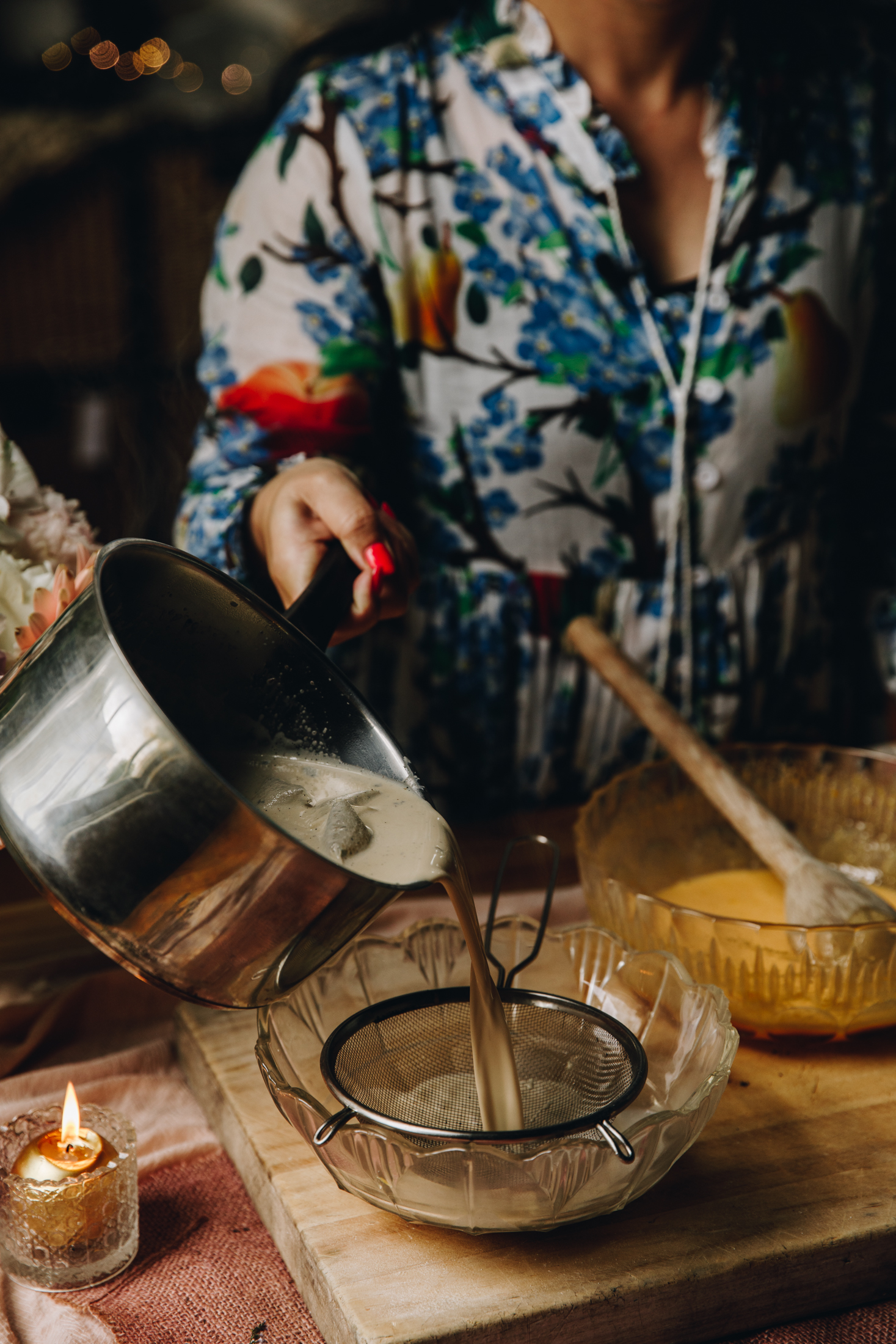 Naomi Toilalo is pouring the cream mixture for chai creme brûlée into a sieve. The egg yolk bowl is behind it in a bowl. They are all on a wooden board. 