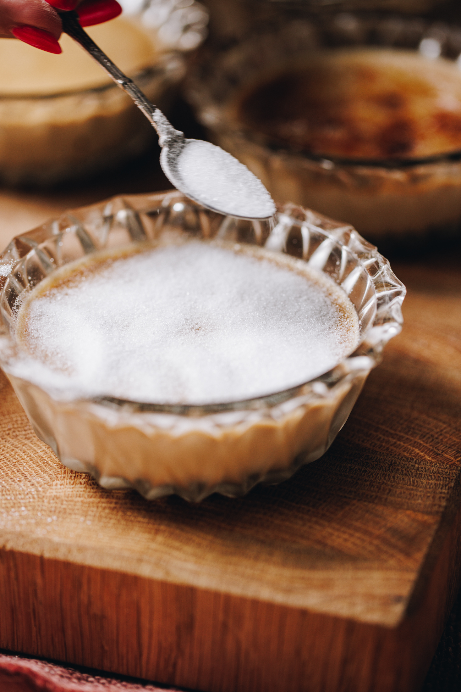 A close up of a baked Chai Créme Brûlée shows a teaspoon sprinkling caster sugar on top of it. 
