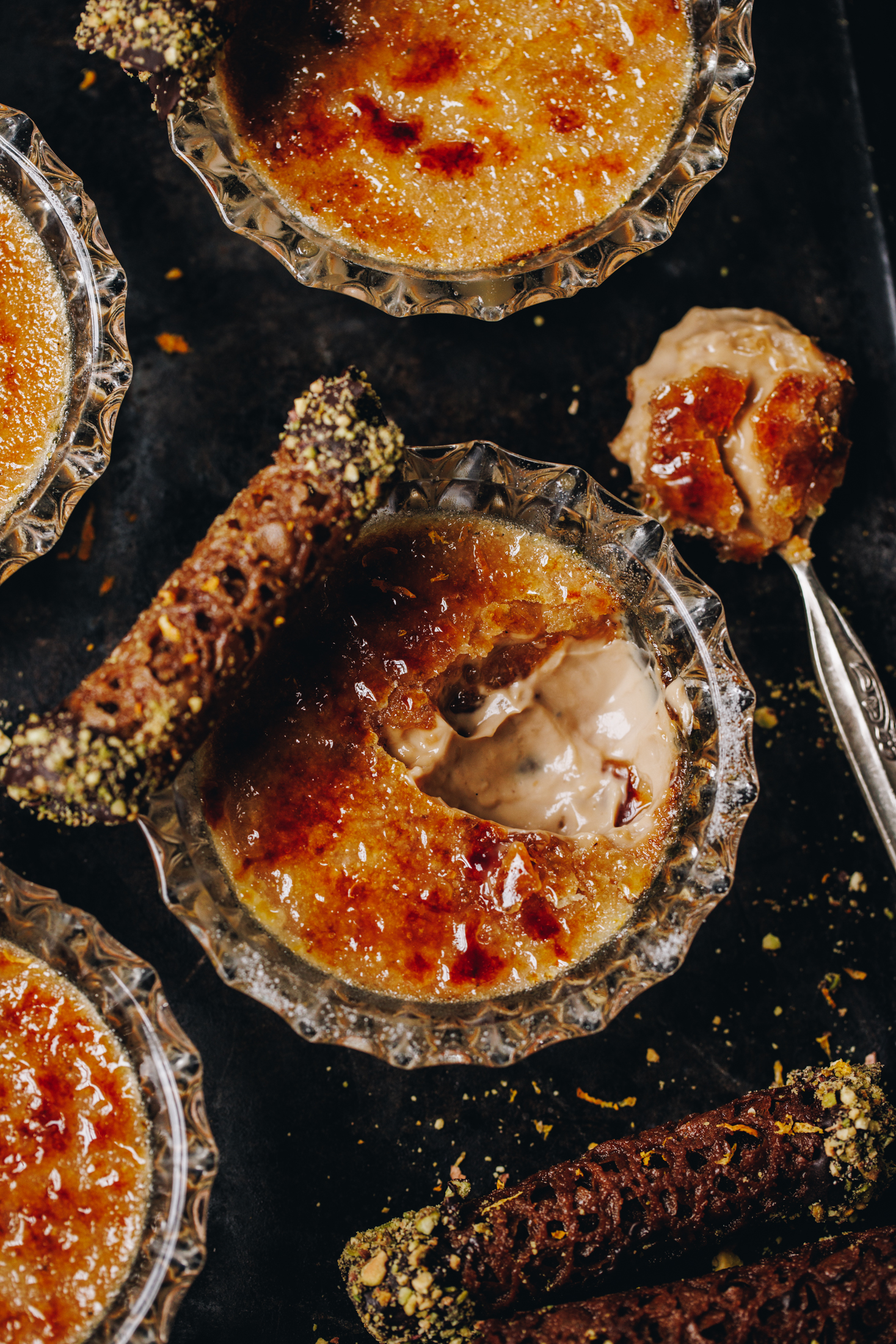 On a black tray is a flat lay of freshly baked chai creme brûlée - one of them has been cracked open, revealing the creamy custard underneath the hard sugar top.