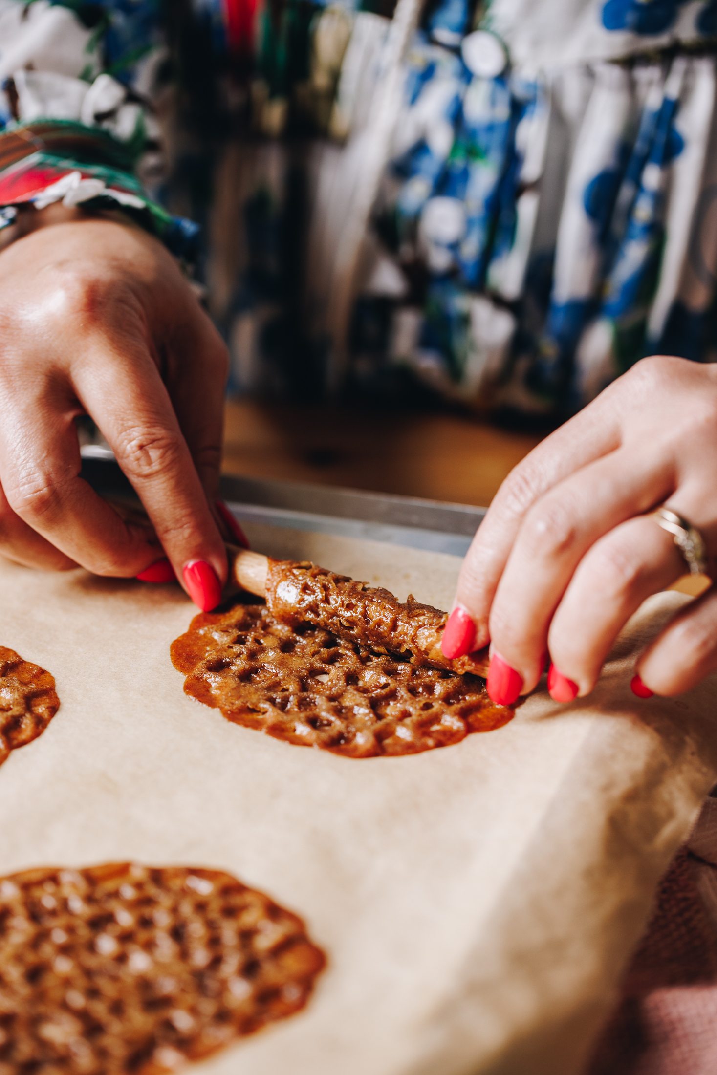 Mini Brandy Snaps are being rolled up with a small wooden handle, freshly baked round discs are seen on the town baking paper.