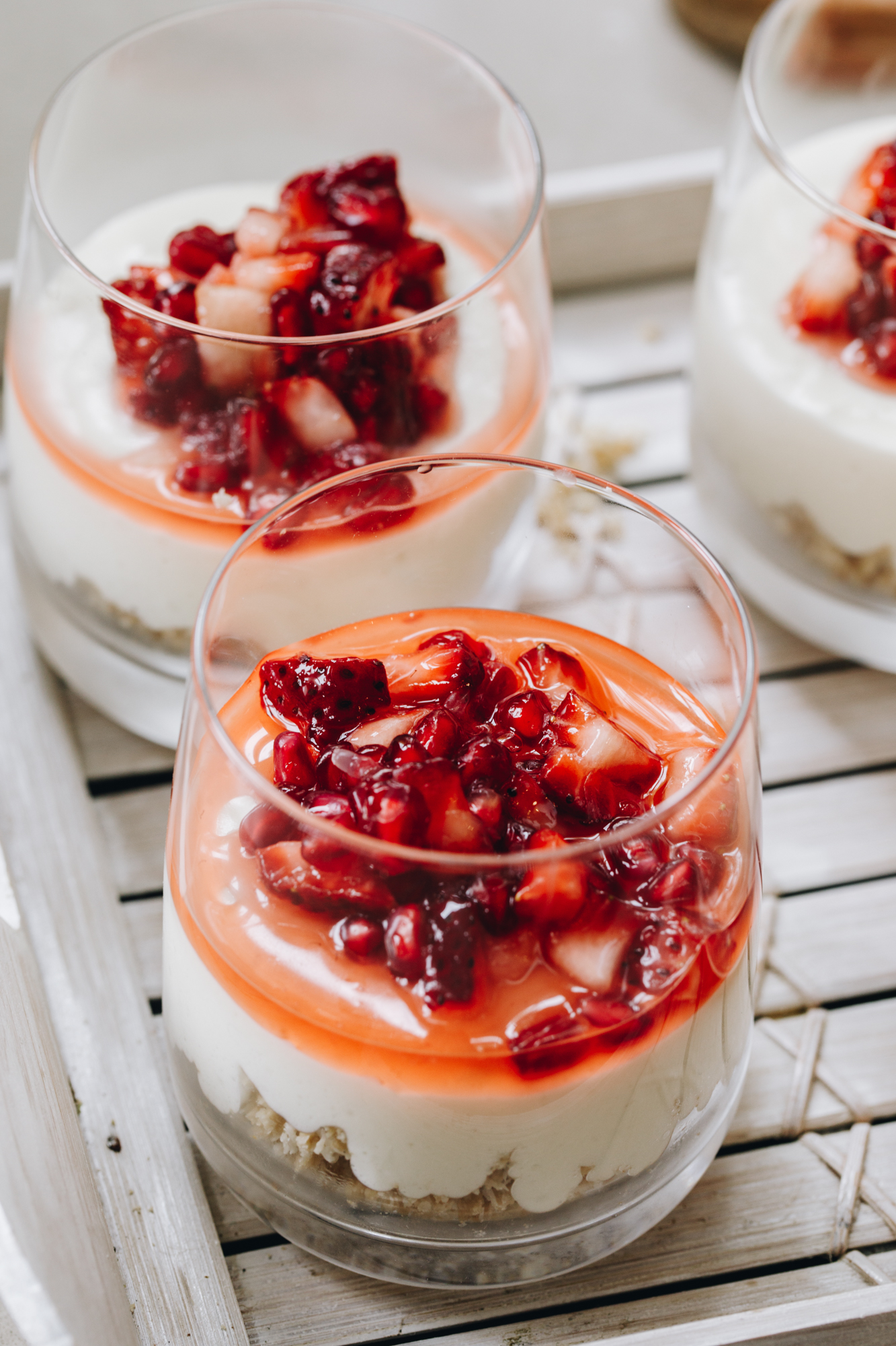 A close shot shows two glasses with the white chocolate mousse in it. In the glasses is a biscuit base, a white chocolate mousse and finely chopped berries with juice.