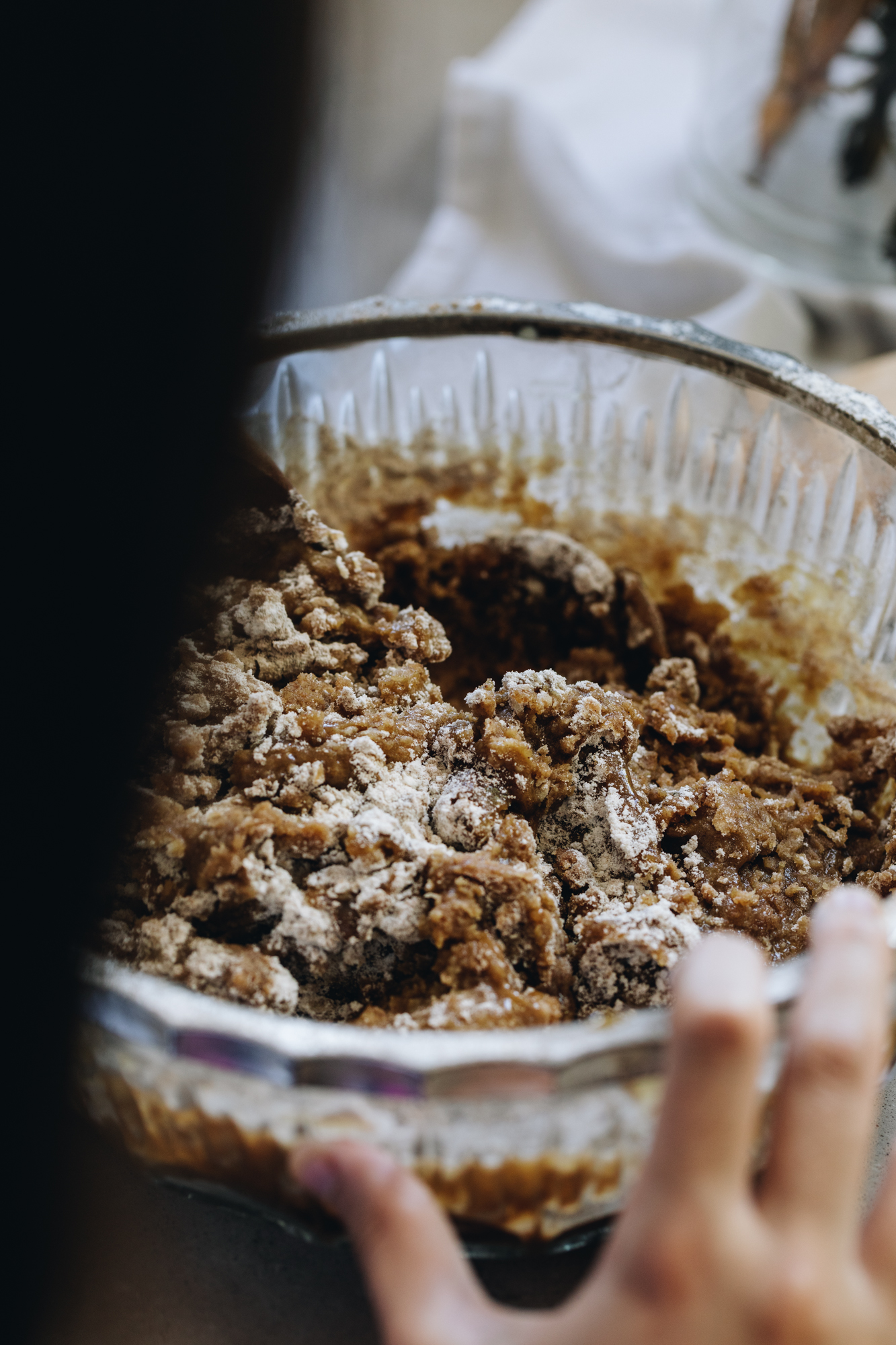 A glass vintage bowl sits on a stone bench. Small kids hands are holding the side of the bowl and inside is gingerbread cookie dough. 