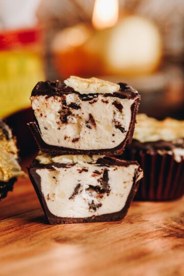 no-bake creamy peppermint cups are cut open and stacked on each other. It shows the creamy peppermint filling. A candle burns in the background with an old school baking tin.
