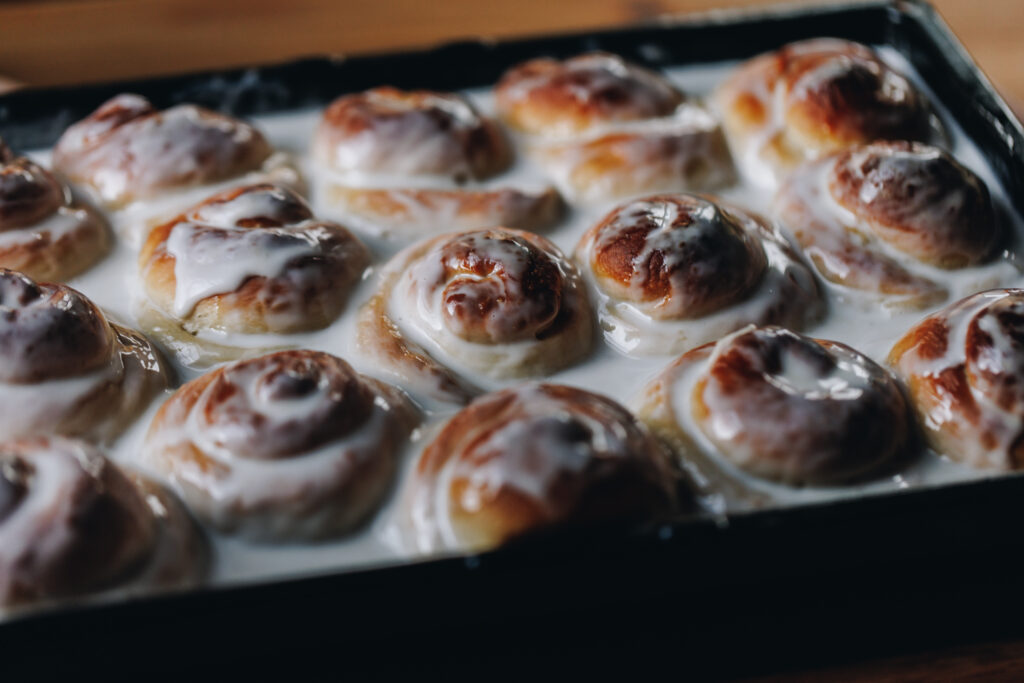 A black baking tray sits on a wooden table. In the tray is freshly baked Pani Popo that are swimming in a coconut sauce.