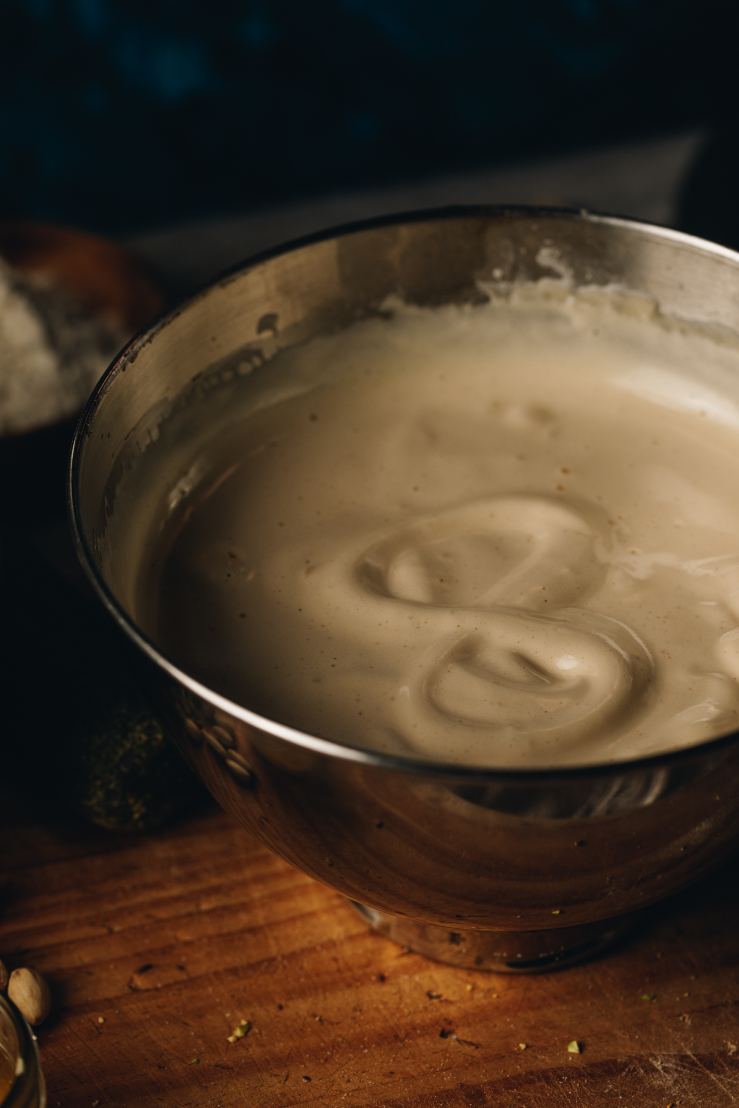 A silver mixing bowl sits on a wooden table. In the bowl is a mixture of whipped eggs that looks fluffy. In the mixture is the shape of a figure 8, showing the whipped eggs are ready. 