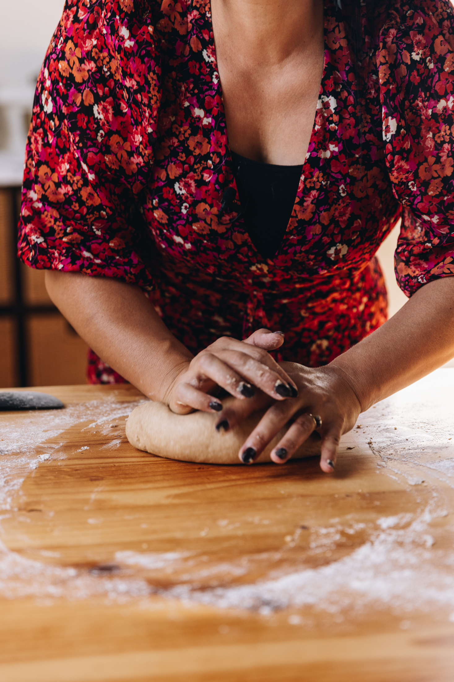 Naomi Toilalo is kneading a bread dough with both of her hands on a lightly floured wooden table.