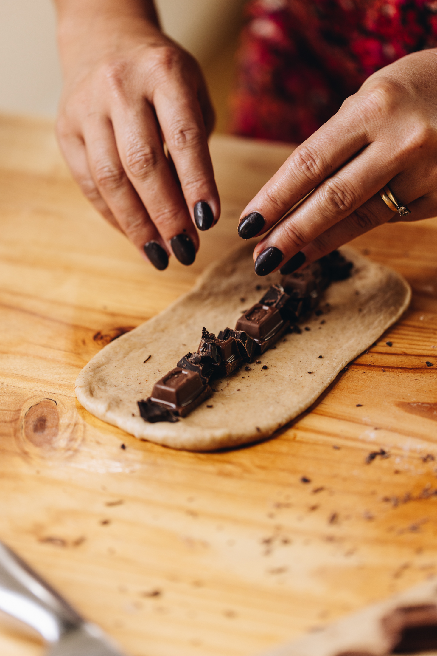 On a wooden table is a rolled out piece of dough that is shaped as a rectangle. Down the centre is chocolate that is arranged down the centre with Naomi's hands in shot.