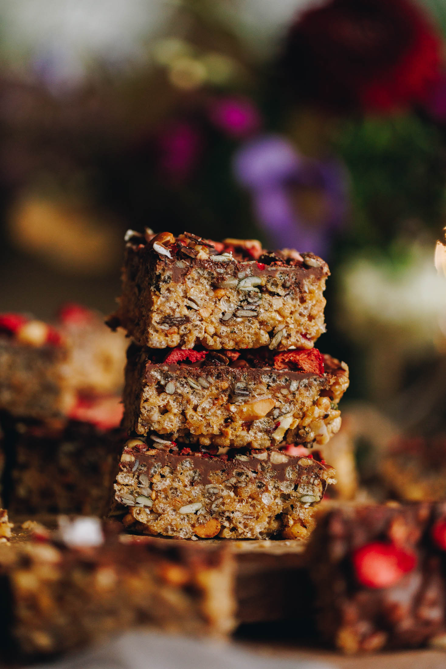 Three pieces of Peanut Butter Rice Bubble Slice are stacked on top of each other in a close shot showing texture and a chocolate topping with freeze-dried strawberries. 