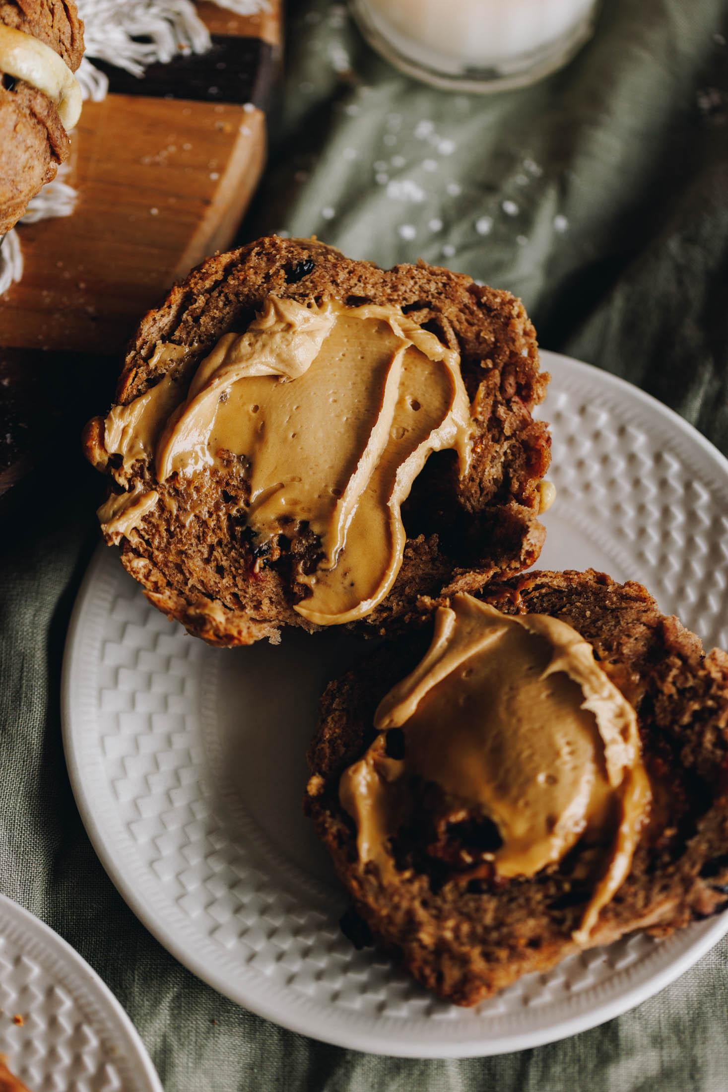 A flat lay shot shows a hot cross bun scone cut open. It has been s[read with whipped biscuit spread and it is starting to melt. The plate is on a green table cloth.