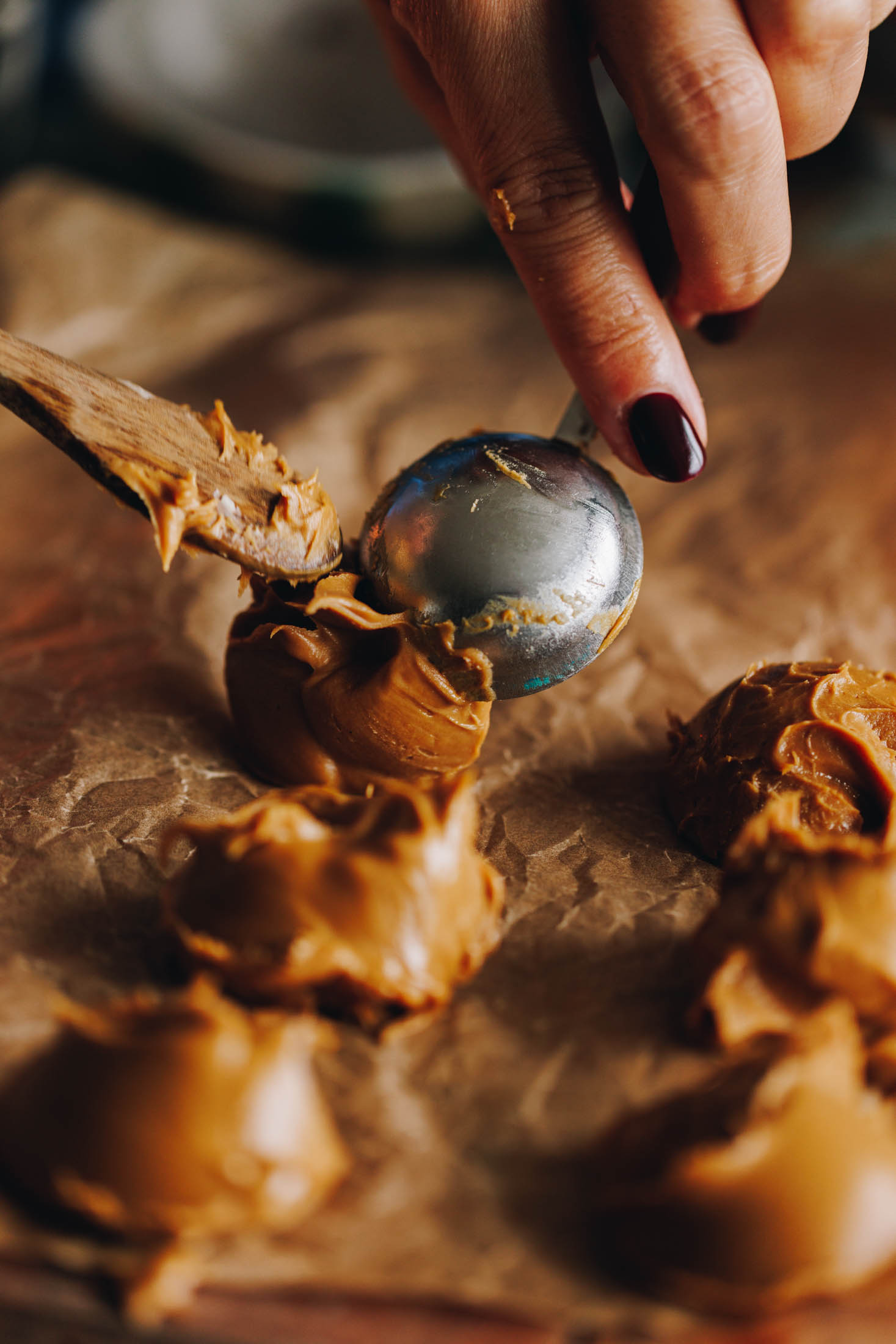 On brown baking paper biscuit spread is being added with a tablespoon and a wooden spoon.