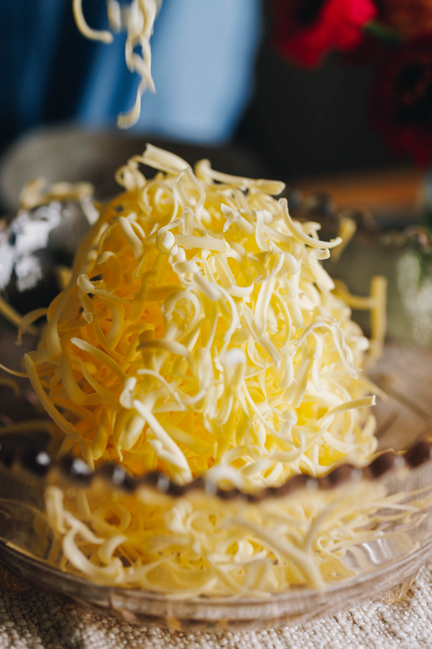 A purple frilled vintage bowl sits on a cream cloth on a wooden table. In the bowl is straws of grate butter that are high in the bowl.