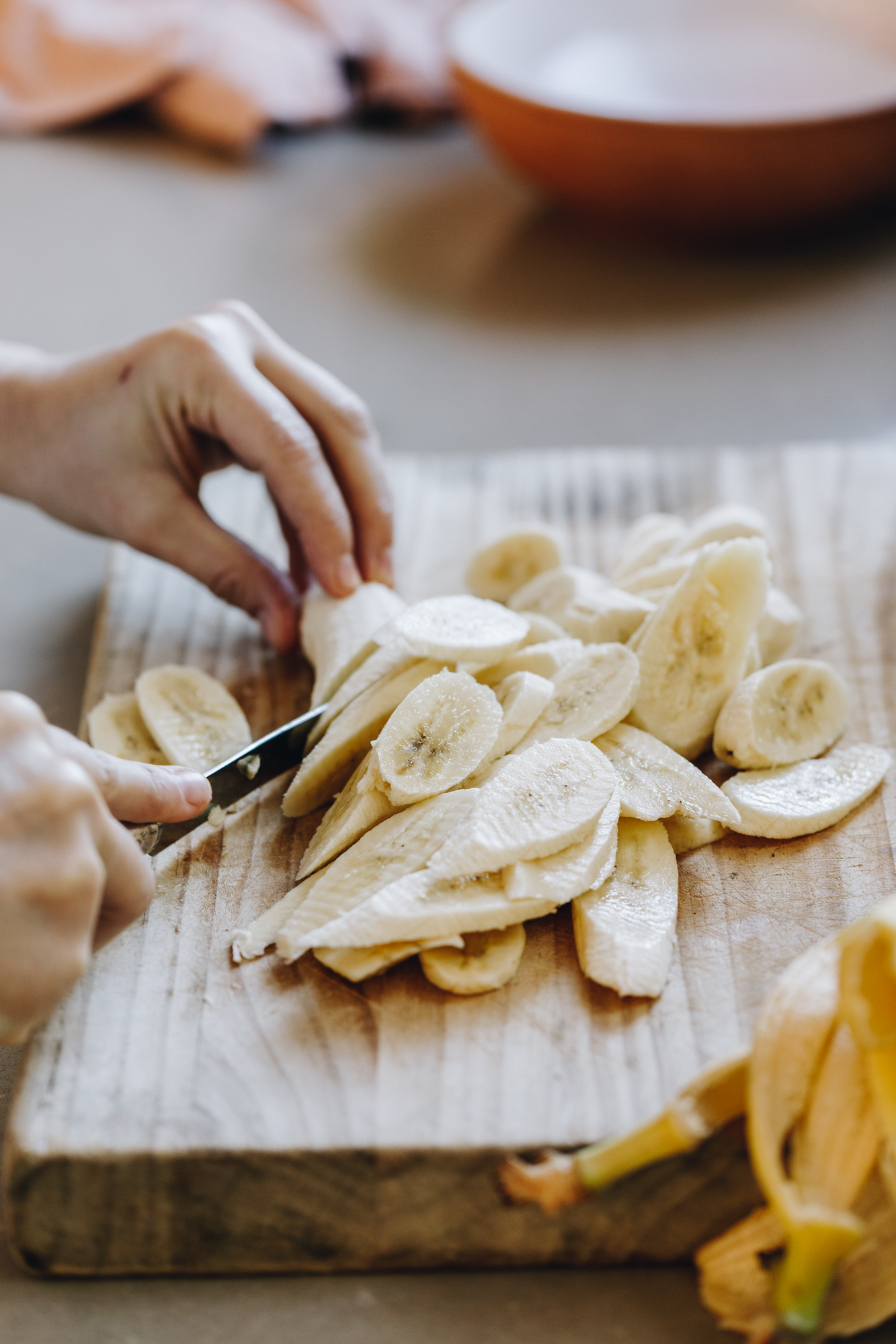 A wooden board has bananas on it that are being sliced in to long pieces. The board is on a grey stone bench.