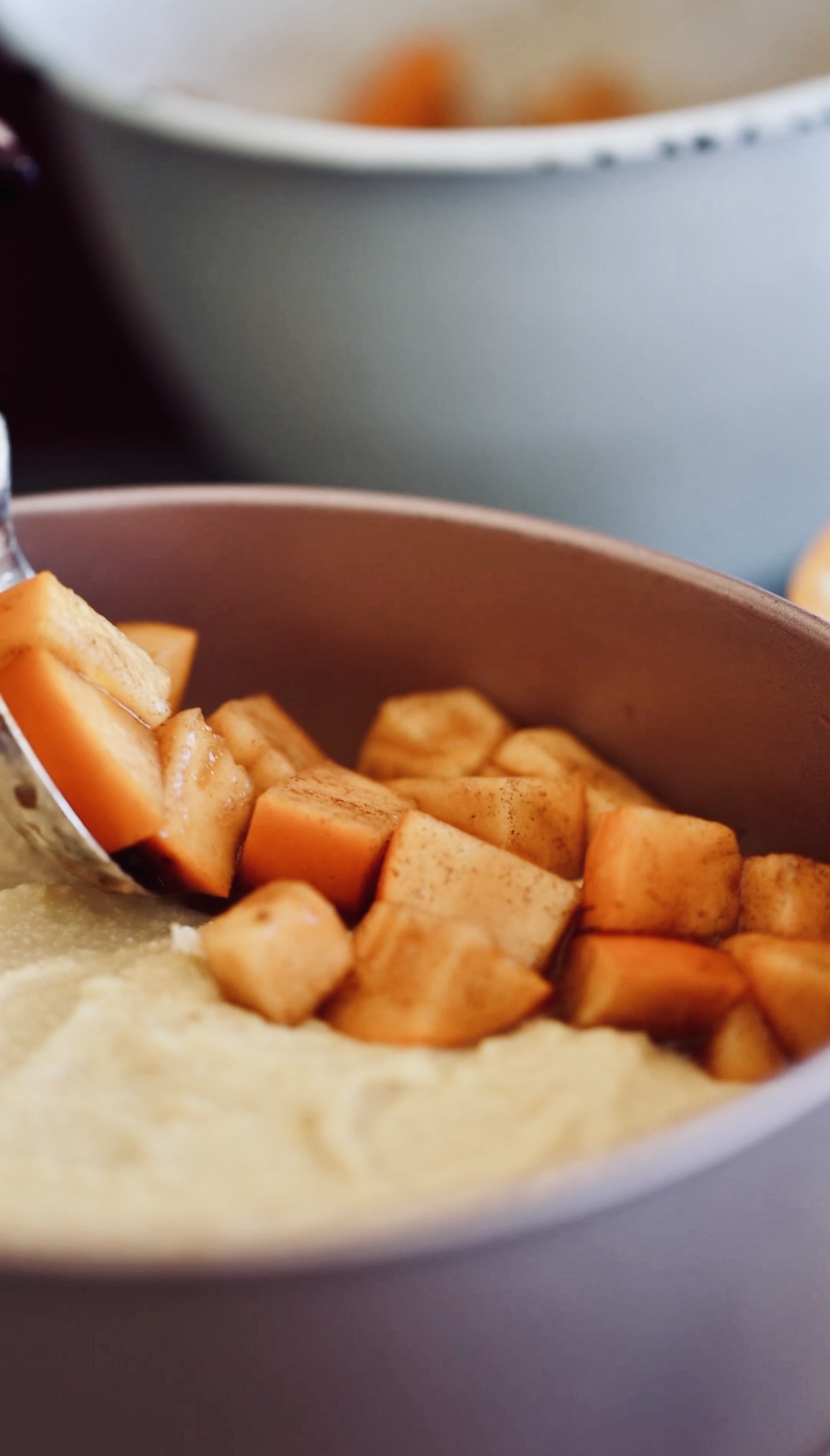 Cubed persimmons are being added on to a cake batter in a rose pink cake tin. 