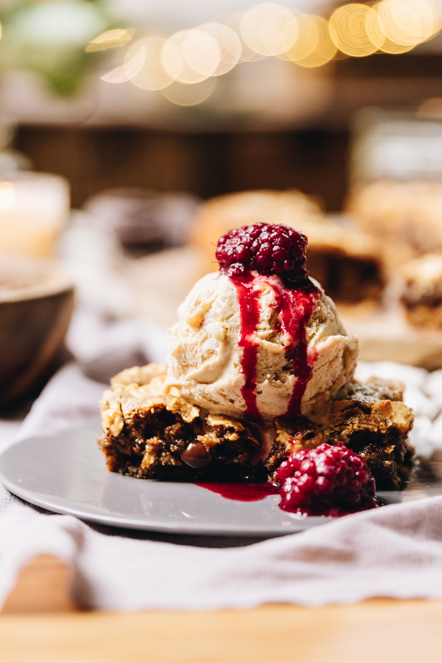 Two pieces of warm coffee chocolate blondie with walnuts on a grey plate, topped with ice cream and drippy canned boysenberries.