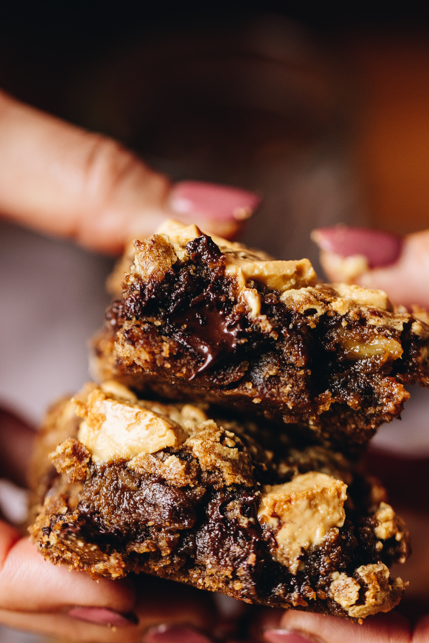 Two slices of chocolate coffee blondies are stacked and held by Naomi's hands, revealing the gooey centre.
