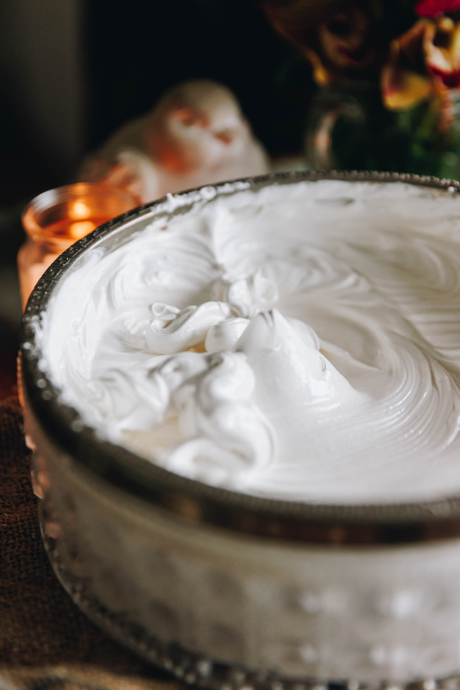 Stiff peak white meringue in a vintage bowl on a wooden board with styling props in the background.