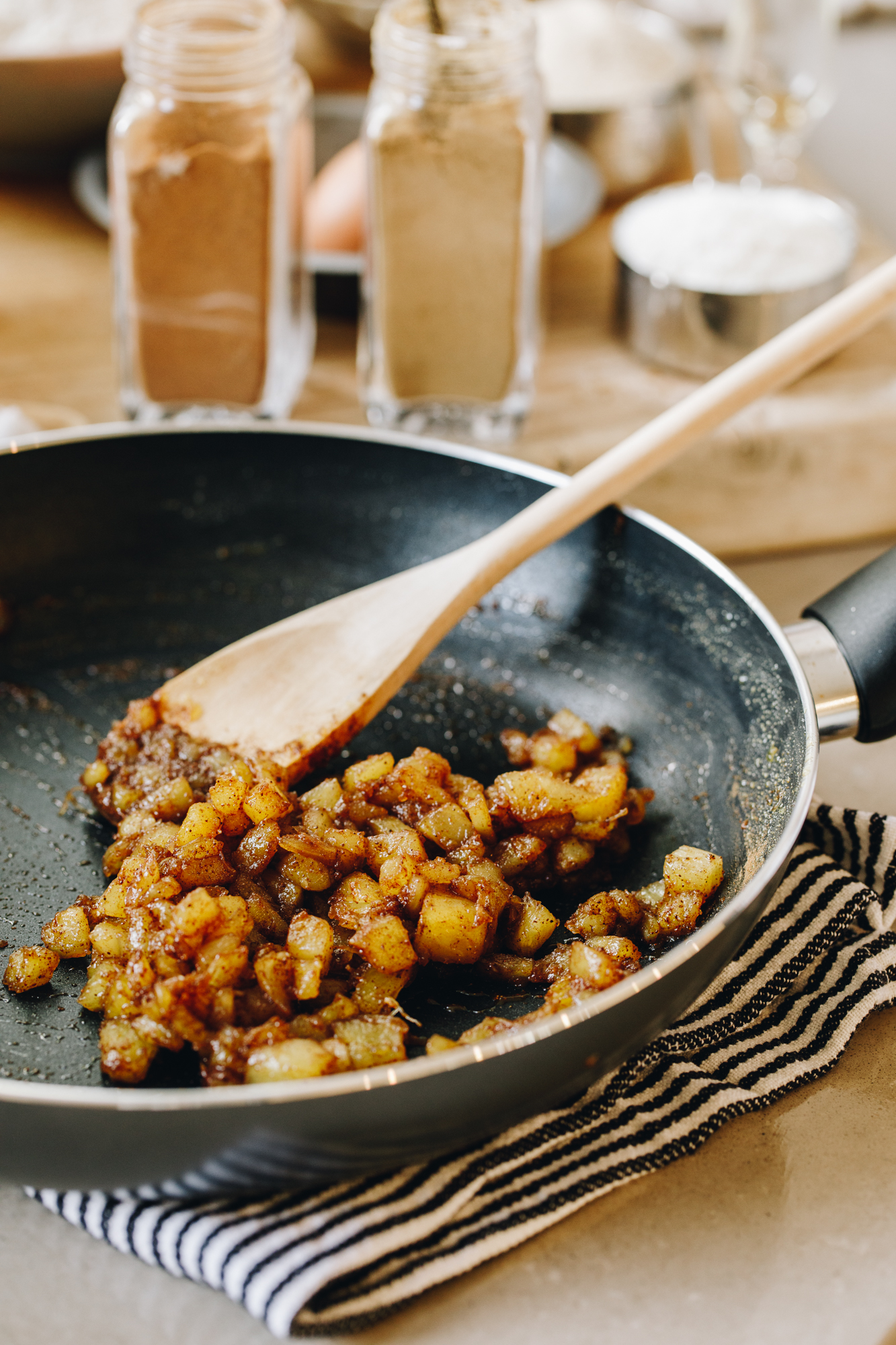Caramelised pineapple in a frying pan with a wooden spoon, spices in the background. 